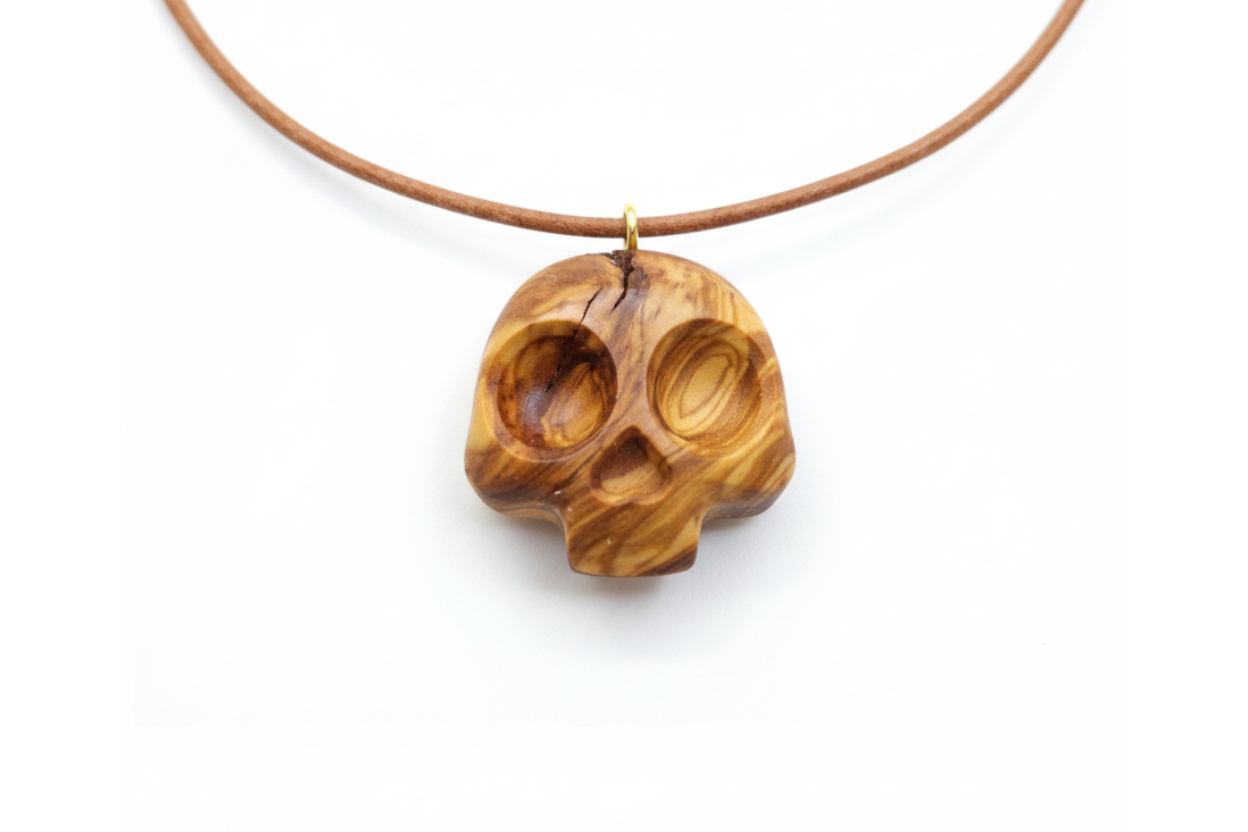 Olive wood skull pendant with warm golden tones and swirling grain on leather cord against white background