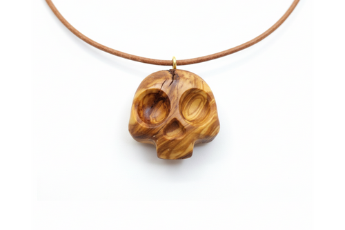 Olive wood skull pendant with warm golden tones and swirling grain on leather cord against white background